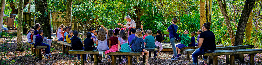 Children and adults sitting on benches listening to a speaker at Boyd Hill Nature Preserve.